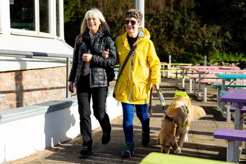 Photo of two people walking, one of whom has a dog on a lead.