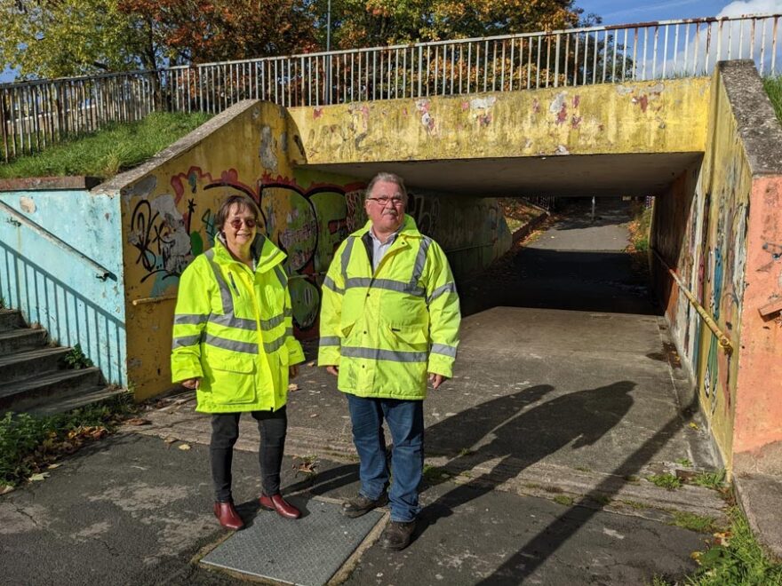 Photo of two people wearing hi-vis jackets standing in the entrance to a subway.