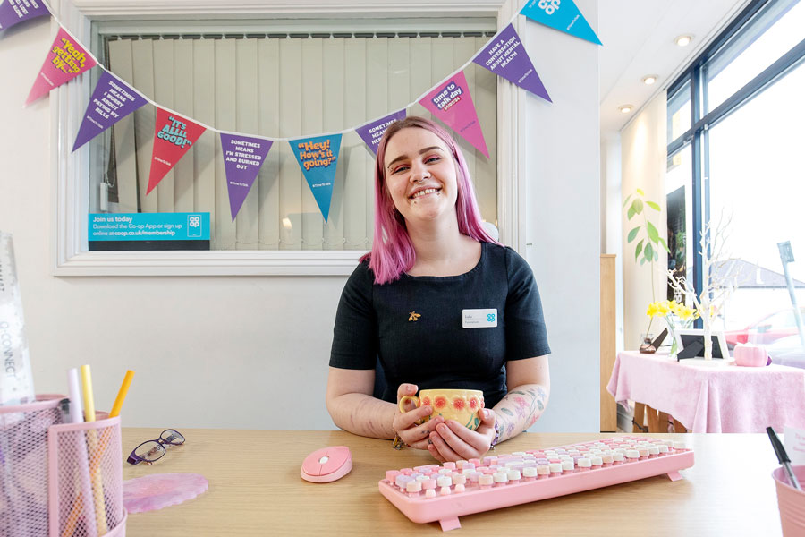 Photo of a young woman sitting behind a desk that has a pink computer keyboard on it.